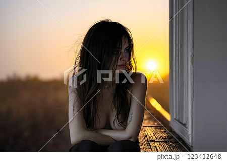 A woman sitting on a window sill looking out at the sunset 123432648