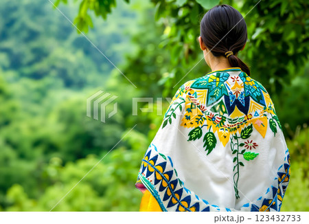 A woman wearing a colorful embroidered shawl standing in front of a lush green forest 123432733