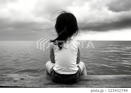 A little girl sitting on a dock looking out at the ocean 123432749