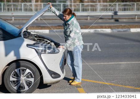 Caucasian woman looks puzzled under the hood of a car.  123433041