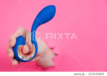Hand with blue vibrator sticking out through pink paper background. Hand with blue vibrator sticking out through pink paper background. 123433065