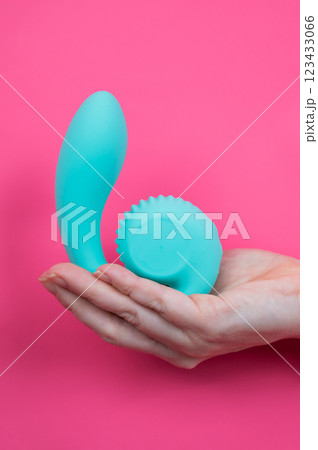 Hand with blue vibrator sticking out through pink paper background. Vertical photo.  123433066