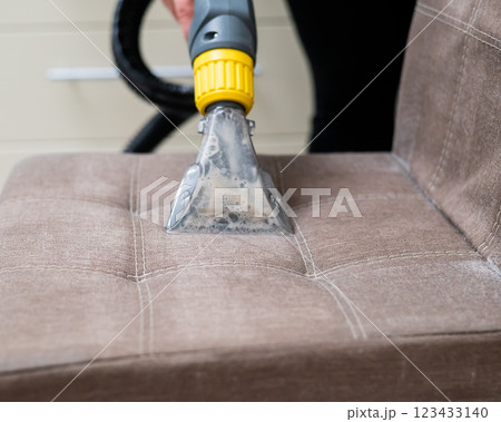 Woman cleaning a fabric chair with a professional washing vacuum cleaner.  123433140
