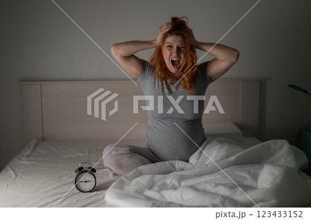 Caucasian pregnant woman sitting in bed and screaming while suffering from insomnia.  123433152