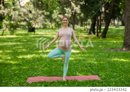 Pregnant caucasian woman doing yoga in the park. Tree pose. 123433342
