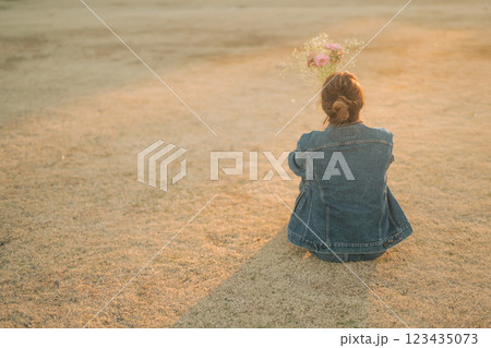 夕方の公園の芝生に座るデニムの女性の後ろ姿 123435073