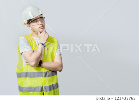 A pensive engineer on white background. Concept of a meditative engineer solated. Pensive builder man with hand on chin, Portrait of young builder thinking with hand on chin isolated 123435765