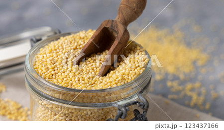 Glass jar of raw uncooked yellow millet grain with a wooden scoop closeup. Ancient food 123437166