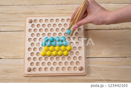 Educational game, wooden board for sorting according to the Montessori system. In his hands are wooden tweezers with a ball. 123442103