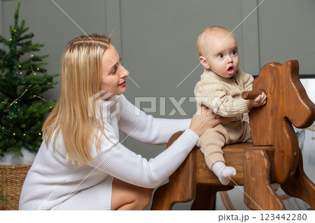 Mom rides her baby on a wooden gurney and horse. 123442280