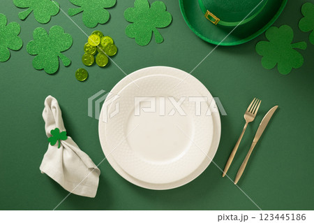 St Patrick's Day table setting with white plate and shamrock, clover leaves and coins on green background. View from above. St Patrick's Day table setting with white plate and shamrock, clover leaves and coins on green background. View from above. 123445186