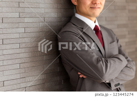 壁にもたれて腕組みをするグレーのスーツを着たミドル男性ビジネスマン 123445274