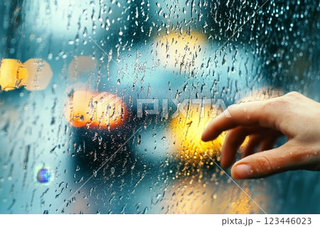 A person gazes sorrowfully out a rain-covered window as a car drives away in the background. 123446023