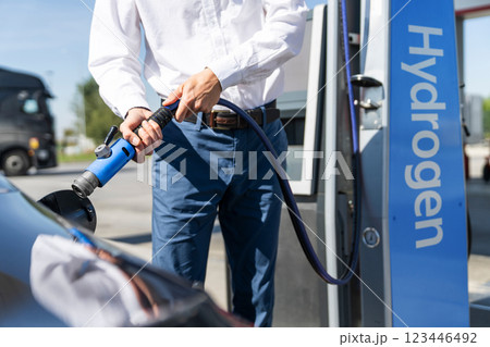 Man holds a hydrogen fueling nozzle on a hydrogen filling station. Refueling car with hydrogen fuel. Man holds a hydrogen fueling nozzle on a hydrogen filling station. Refueling car with hydrogen fuel. 123446492