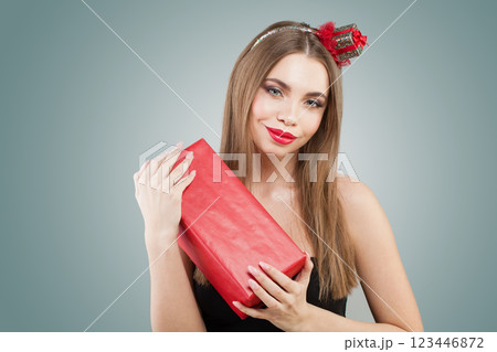 Beautiful young happy woman holding gift present box on grey studio wall background Beautiful young happy woman holding gift present box on grey studio wall background 123446872