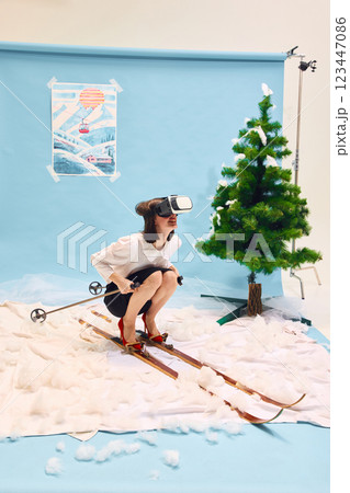 Woman in business clothes wearing VR headset sitting on skis against abstract winter background. 123447086