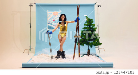 Young woman in gold swimsuit and ski boots confidently standing against winter-themed backdrop. Young woman in gold swimsuit and ski boots confidently standing against winter-themed backdrop. 123447103
