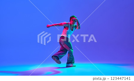 Dynamic image of male performance, breakdance in casual attire in motion against gradient blue purple background in neon light Dynamic image of male performance, breakdance in casual attire in motion against gradient blue purple background in neon light 123447141