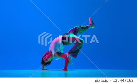 Dynamic image of young artistic man, break dancer in casual clothes in motion on stage, dancing against gradient blue purple background in neon light Dynamic image of young artistic man, break dancer in casual clothes in motion on stage, dancing against gradient blue purple background in neon light 123447162