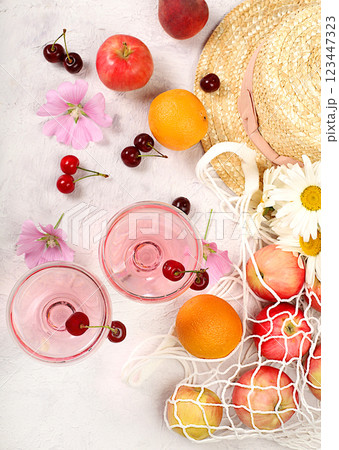 Summer fashion banner on a bright background. Straw hat, fruits in an eco-bag, refreshing alcoholic drinks and chamomile flowers on a sunny table. Vacation and travel concept, outdoor camping and 123447323