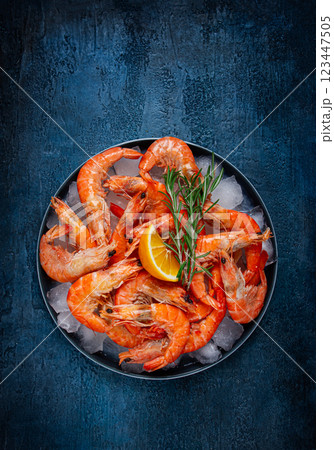 Freshly frozen shrimp on ice, with lemon and rosemary, on a dark blue table, top view, no people 123447505