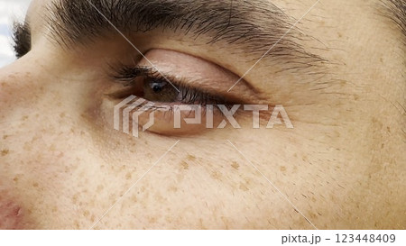 Focus on left brown eye of handsome sorrowful man looking into the distance. Portrait of unhappy male face with freckles outdoor. Upset facial expression of young guy. Close up Focus on left brown eye of handsome sorrowful man looking into the distance. Portrait of unhappy male face with freckles outdoor. Upset facial expression of young guy. Close up 123448409
