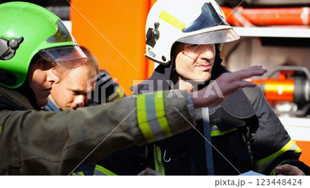 Male firefighters in protective uniforms discuss rescue plan looking at paper instructions near fire truck. Young firemen prepare to extinguishing fire against the background of big red car. Slow mo Male firefighters in protective uniforms discuss rescue plan looking at paper instructions near fire truck. Young firemen prepare to extinguishing fire against the background of big red car. Slow mo 123448424