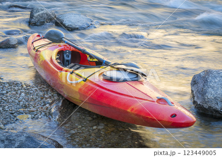whitewater kayak on a river shore with a rapid in background 123449005