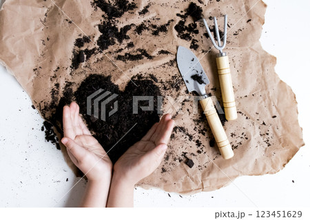 Child hands shaping soil heart with garden tools on brown paper Child hands shaping soil heart with garden tools on brown paper 123451629