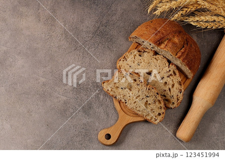 Freshly baked homemade bread, whole grain sourdough bread with a crispy crust, sliced and ears of rye and wheat on a concrete background with space for text, modern baking concept, healthy natural 123451994