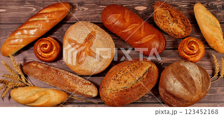 Freshly baked bakery products, whole grain homemade bread, different types of round sourdough bread with crispy crust, baguettes, buns and ears of wheat on wooden background, modern baking concept 123452168