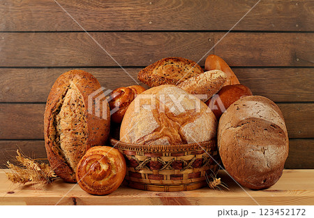 Whole grain homemade bread, different types of round sourdough bread with crispy crust, baguettes, buns and wheat ears, freshly baked bakery products on wooden background, modern baking concept, 123452172