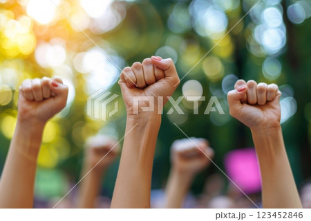 Participants in a peaceful protest raise their fists in solidarity showcasing determination and unity. The setting is a lush park filled with trees during early afternoon light. 123452846