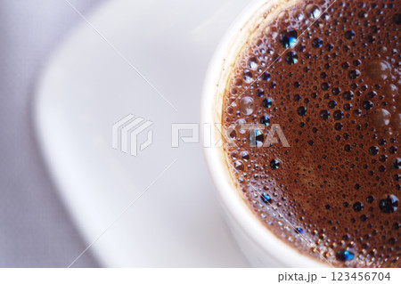 Dark steaming coffee cup placed on a white saucer in a cafe 123456704