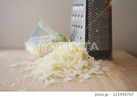 Shredded cheese beside a grater on a wooden kitchen counter Shredded cheese beside a grater on a wooden kitchen counter 123456707