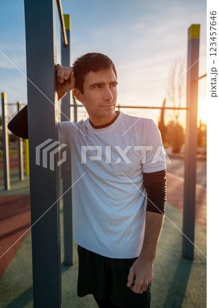 young athletic man resting after fitness calisthenics workout at street gym during sunset, taking a break during body improvement and strength training 123457646