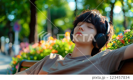 明るい公園のベンチで目を閉じてヘッドフォンで音楽を聴く若い男性 明るい公園のベンチで目を閉じてヘッドフォンで音楽を聴く若い男性 123457834