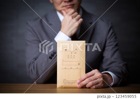 グレーのスーツを着て給料袋を持って悩むミドル男性ビジネスマン 123459055
