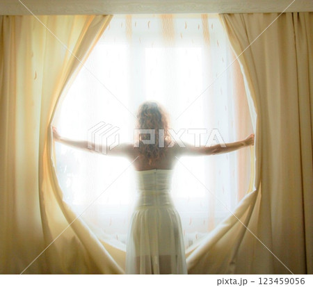 girl opening curtains in a bedroom 123459056