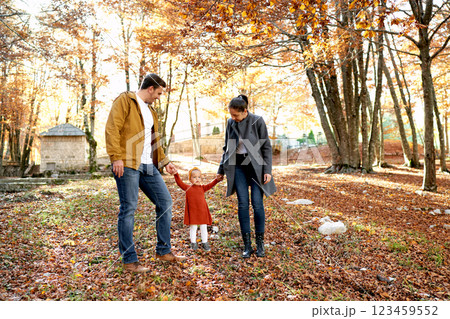 Mom and dad look at a little girl, holding her hands in the autumn forest Mom and dad look at a little girl, holding her hands in the autumn forest 123459552