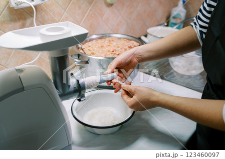 Housewife puts an intestine on a sausage attachment on an electric meat grinder Housewife puts an intestine on a sausage attachment on an electric meat grinder 123460097