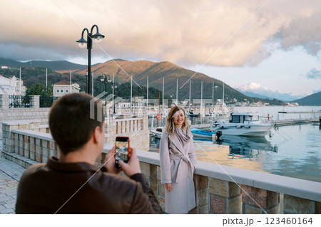 Guy shoots girl at the fence of the embankment with moored yachts against the backdrop of the mountains at sunset. Back view Guy shoots girl at the fence of the embankment with moored yachts against the backdrop of the mountains at sunset. Back view 123460164