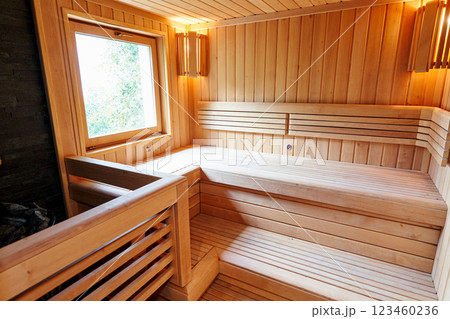 Wooden benches in the sauna with lamps in the corners near the window opposite the stove Wooden benches in the sauna with lamps in the corners near the window opposite the stove 123460236