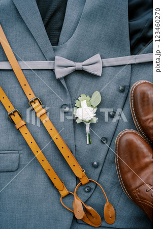Leather suspenders, men shoes and a boutonniere lie on the groom suit Leather suspenders, men shoes and a boutonniere lie on the groom suit 123460270