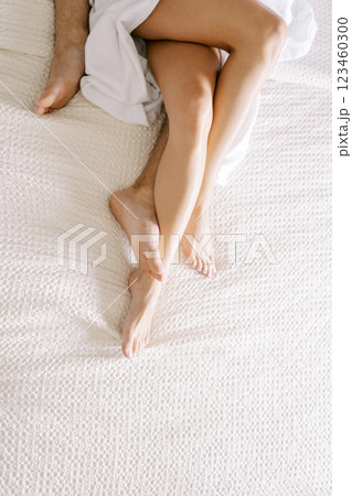 Woman bare feet covered with a bathrobe lie on man legs on the bed. Cropped. Faceless 123460300
