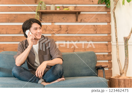 自宅のソファに座りスマホで通話する若いアジア人男性 123462475