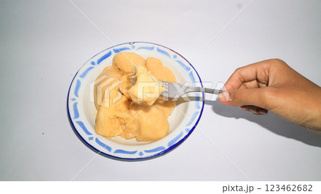 An Asian woman's hand holding a fork picks up cassava tape on a plate. Indonesia food. An Asian woman's hand holding a fork picks up cassava tape on a plate. Indonesia food. 123462682