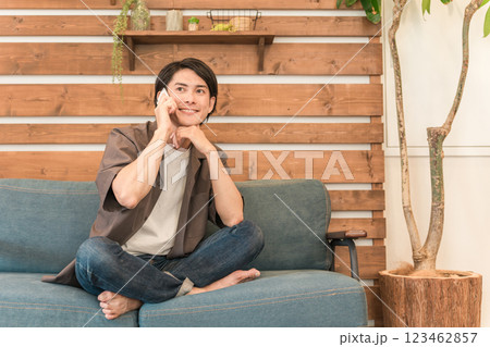 自宅のソファに座りスマホで通話する若いアジア人男性 自宅のソファに座りスマホで通話する若いアジア人男性 123462857