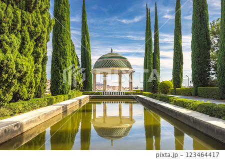 The Historical Botanical Garden La Concepcion in Malaga city at Andalusia, Spain, Europe. Serene garden gazebo reflected in a tranquil pond, surrounded by lush greenery and tall trees. 123464417