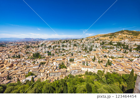 Granada town in Spain. Panoramic view of a city nestled against a hill, under a vibrant blue sky. Buildings with terracotta roofs stretch as far as the eye can see. 123464454